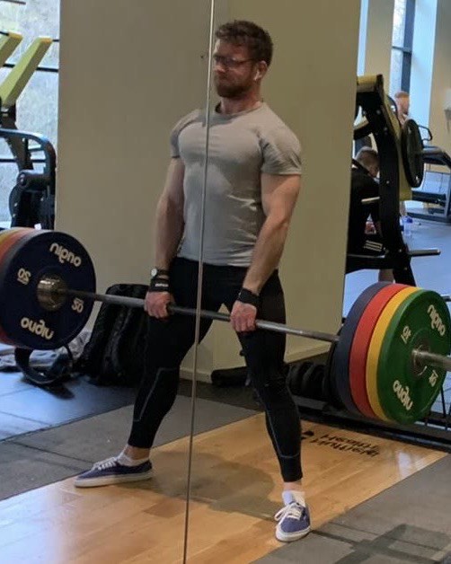 Balazs Morvay standing tall at the top of a deadlift, barbell at his hips
